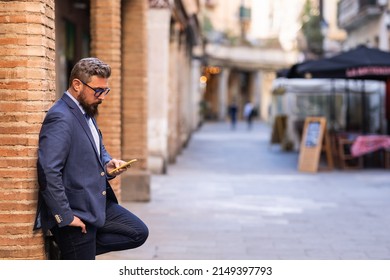 Businessman using a mobile phone while leaning on a column outdoors in the street.