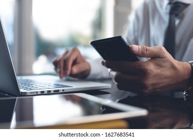 Businessman Using Mobile Smart Phone While Working On Laptop Computer With Digital Tablet On Desk. Business Man Connecting Internet, Networking In Modern Office, Closeup