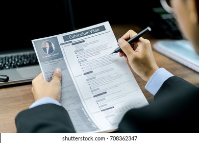 Empresario que usa el bolígrafo para revisar o revisar el Curriculum Vitae o CV del candidato antes de entrevistar con un portátil y teléfono en la mesa de madera en segundo plano