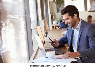 Businessman Using Phone Whilst Working In Coffee Shop