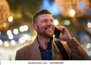 Businessman using smartphone having phone call talking on mobile phone in city evening with lights in background