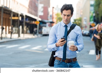 Businessman using smartphone and holding paper cup ina urban scene. Worried businessman walking on the road and messaging with phone.
 - Powered by Shutterstock