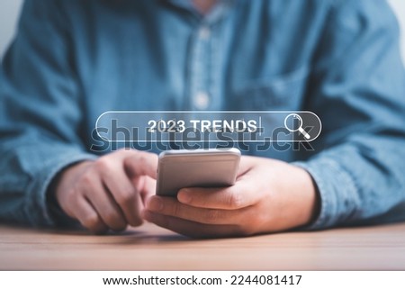 Businessman using smartphone to input keyword of 2023 trends inside infographic searching  tool bar for marketing monitor and business planing change concept.