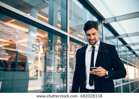 Businessman using smartphone and smiling at airport. Young business executive with mobile phone at airport.