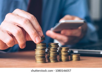 Businessman using smartphone with stacked coins in foreground, close up shot with selective focus - Shutterstock ID 1080146057