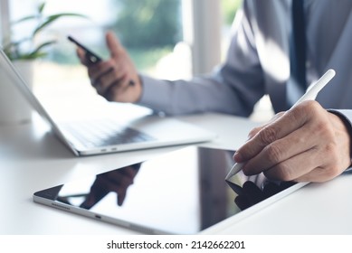 Businessman using stylus pen signing e-document on digital tablet during working on laptop computer and using mobile smartphone on office table. Man project manager at work at office