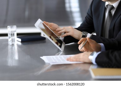 Businessman using tablet computer and work together with his colleague or partner at the glass desk in modern office, close-up. Unknown business people at meeting. Teamwork and partnership concept