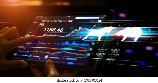 A businessman using a tablet mobile device to check and analyzing market data with bull and bear shapes symbols of stock market trends on them, stock market exchange on interface virtual screen.
