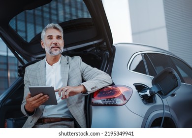 Businessman using tablet while charging car at electric vehicle charging station, closeup. - Powered by Shutterstock