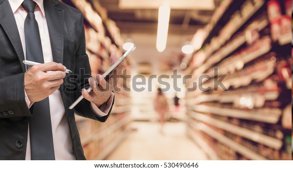Businessman using\
the tablet and writing the order stock on Supermarket blur\
background, business technology\
concept