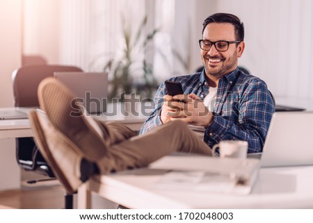 Businessman usning smart phone in the office with legs on the desk