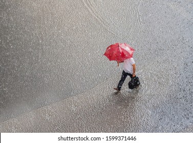 businessman in a very heavy rain walks down the street. He is holding bag and red umbrella in hand.  - Powered by Shutterstock