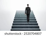 Businessman walking up a concrete staircase towards a bright, white background. Concept of career advancement, success, and ambition