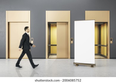 Businessman Walking In Grey Concrete Interior With Three Elevator Doors And Empty Mockup Poster. Opportunity And Success Concept