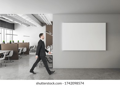 Businessman Walking In Modern Office With Computers And Horizontal Poster On Wall. Workplace And Corporate Concept.