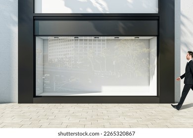 Businessman walking through sunlit empty showcase with light wall background behind window with space for product presentation in modern business center building outdoors, mock up