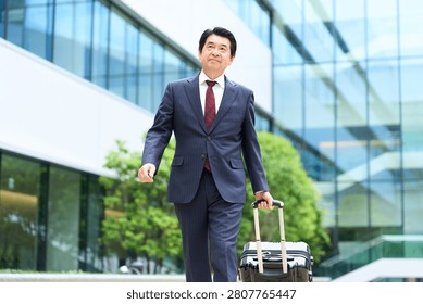 A businessman walking while pulling a suitcase.