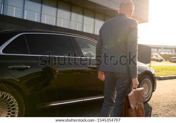businessman walks on the background of a building and a\
car 