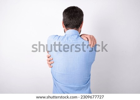 businessman wearing blue shirt holding a piggy bank  over white background hugging herself happy and positive from backwards. Self love and self care