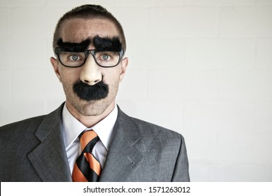 Businessman Wearing A Disguise Of Glasses With Thick Eyebrows And Mustache Looking At Camera With Blank Expression