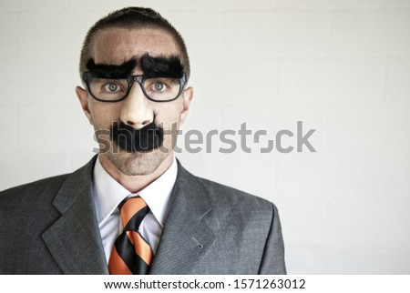 Businessman wearing a disguise of glasses with thick eyebrows and mustache looking at camera with blank expression