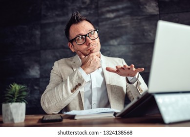 Businessman Wearing Linen Suit And Eyeglasses Standing At His Desk By The Window And Rating Current State Of Business With Hand Gestures During Video Call