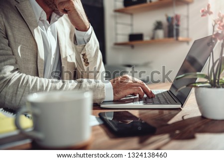 Businessman wearing linen suit sitting at his desk and using laptop in the office
