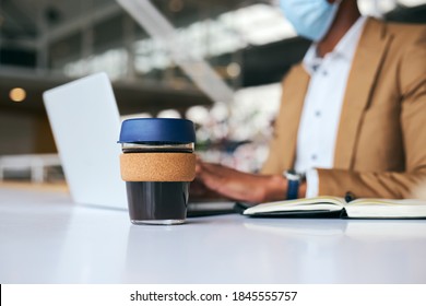 Businessman Wearing Mask With Reusable Coffee Cup Works On Laptop At Desk In Office During Pandemic