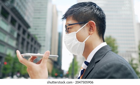 A businessman wearing a surgical mask for hands-free calling on a smartphone. - Powered by Shutterstock