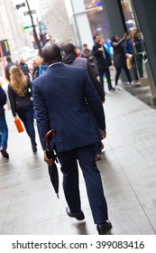Businessman wearing umbrella, walking crowded sidewalk of Manhattan, New York City, United States of America.