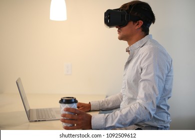 Businessman wearing virtual reality, augmented reality black glasses. Young man working on grey laptop, with cup of coffee. Inside the room, can be home or living room. - Powered by Shutterstock