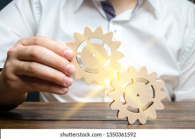 Businessman in white shirt connects two wooden gears. Symbolism of establishing business processes and communication. Increase efficiency and productivity. The best business formula for success.