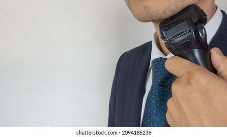 A businessman who shave his beard with an electric shaver. - Shutterstock ID 2094185236
