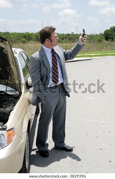 A businessman whose care has
broken down in a remote location checking for phone
signal.
