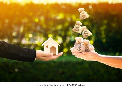 Businessman and woman hand holding a model home and money bag presenting to each other in the public park, Saving money for buy a new house or loan for plan business investment of real estate concept.