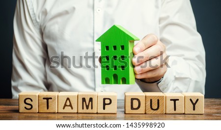 Businessman and wooden blocks with the word Stamp duty and house. Taxes assessed during the transfer of real estate between two parties. Buying housing and land. Property. Stamp Duty Land Tax SDLT