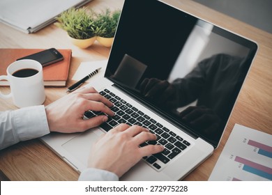 Businessman at work. Close-up top view of man working on laptop while sitting at the wooden desk  - Powered by Shutterstock