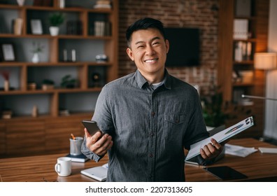 Businessman Work At Home. Glad Successful Middle Aged Chinese Male With Tablet And Phone In Office Interior. Business And Freelance With App, Great Offer And Ad, Startup And Trade Remote Due Covid-19