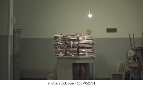 Businessman working behind a lot of stacked paperwork on his desk in a rundown office with cheap furniture