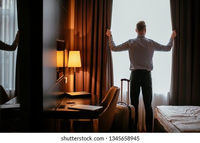 Businessman working from hotel. Guy opening the curtains at the hotel room. - Powered by Shutterstock