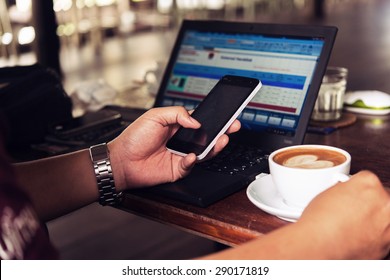 Businessman Is Working With Laptop, Holding A Mobile Phone In Coffe Shop And Drinking Coffe.