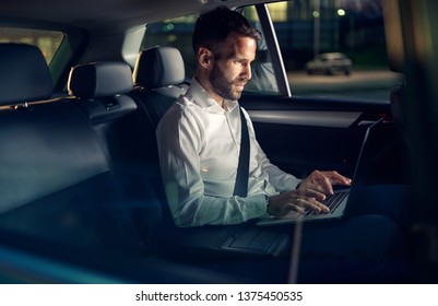 Businessman Working Late In Car On Laptop In Back Seat
