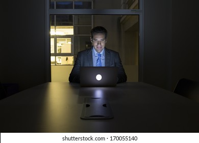Businessman Working Late In His Office On Laptop, Night Light Building Background 