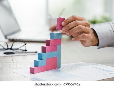 Businessman Working At Office Desk, He Is Building A Growing Financial Graph Using Wooden Toy Blocks: Successful Business Concept