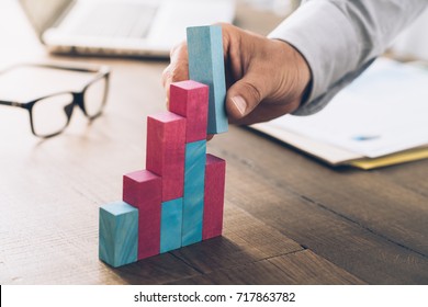 Businessman working at office desk, he is building a growing financial graph using wooden toy blocks: successful business concept - Shutterstock ID 717863782