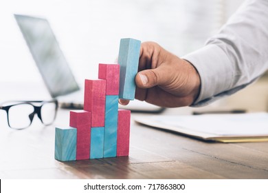 Businessman working at office desk, he is building a growing financial graph using wooden toy blocks: successful business concept