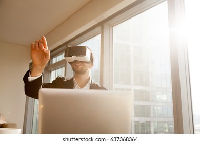 Businessman working in office with virtual reality glasses on head. Man using VR headset for editing project or document in augmented reality. Entrepreneur interacts with three-dimensional simulation - Powered by Shutterstock