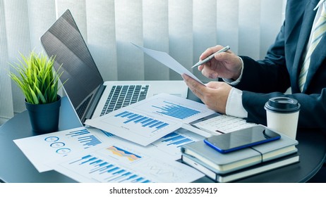 Businessman working on graph papers and laptops using income and expense calculators, accounts or financial auditors to make reports, calculations, home finance, investment, economy, savings or office