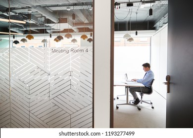 Businessman Working On Laptop At Boardroom Table Viewed Through Meeting Room Door