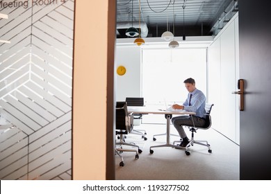 Businessman Working On Laptop At Boardroom Table Viewed Through Meeting Room Door